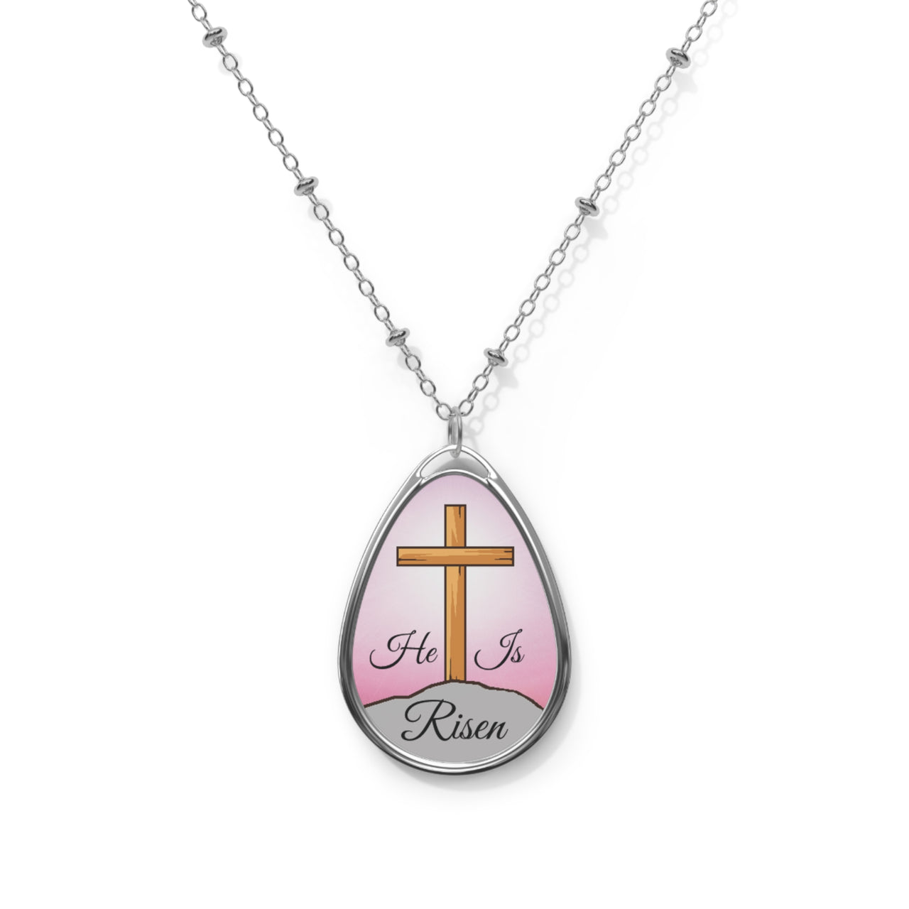 Inspirational oval pendant necklace with "He Is Risen" design,  cross on a hill artwork, zinc alloy and white aluminum, spiritual jewelry for resurrection faith, pink sky, front