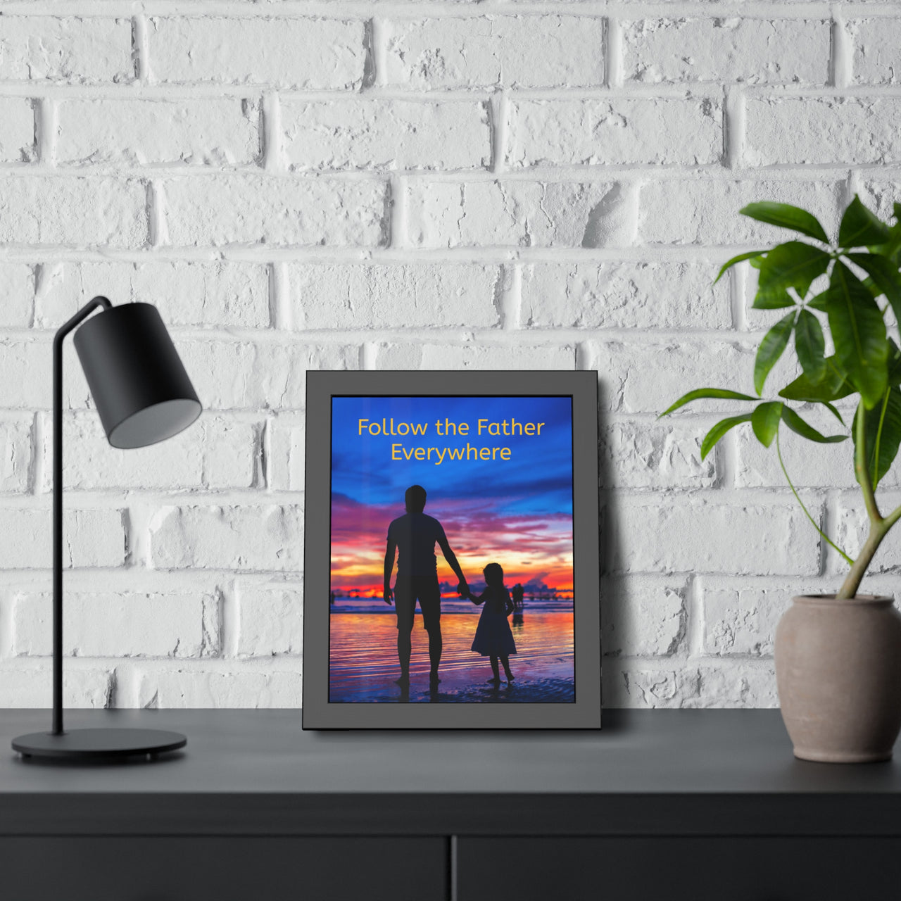 Black wood framed inspirational poster with “Follow the Father” design, child walking with father with the message "Follow the Father Everywhere," semi-gloss finish, shatter-proof plexiglass, available in 3 sizes, 11x14 framed poster at desk