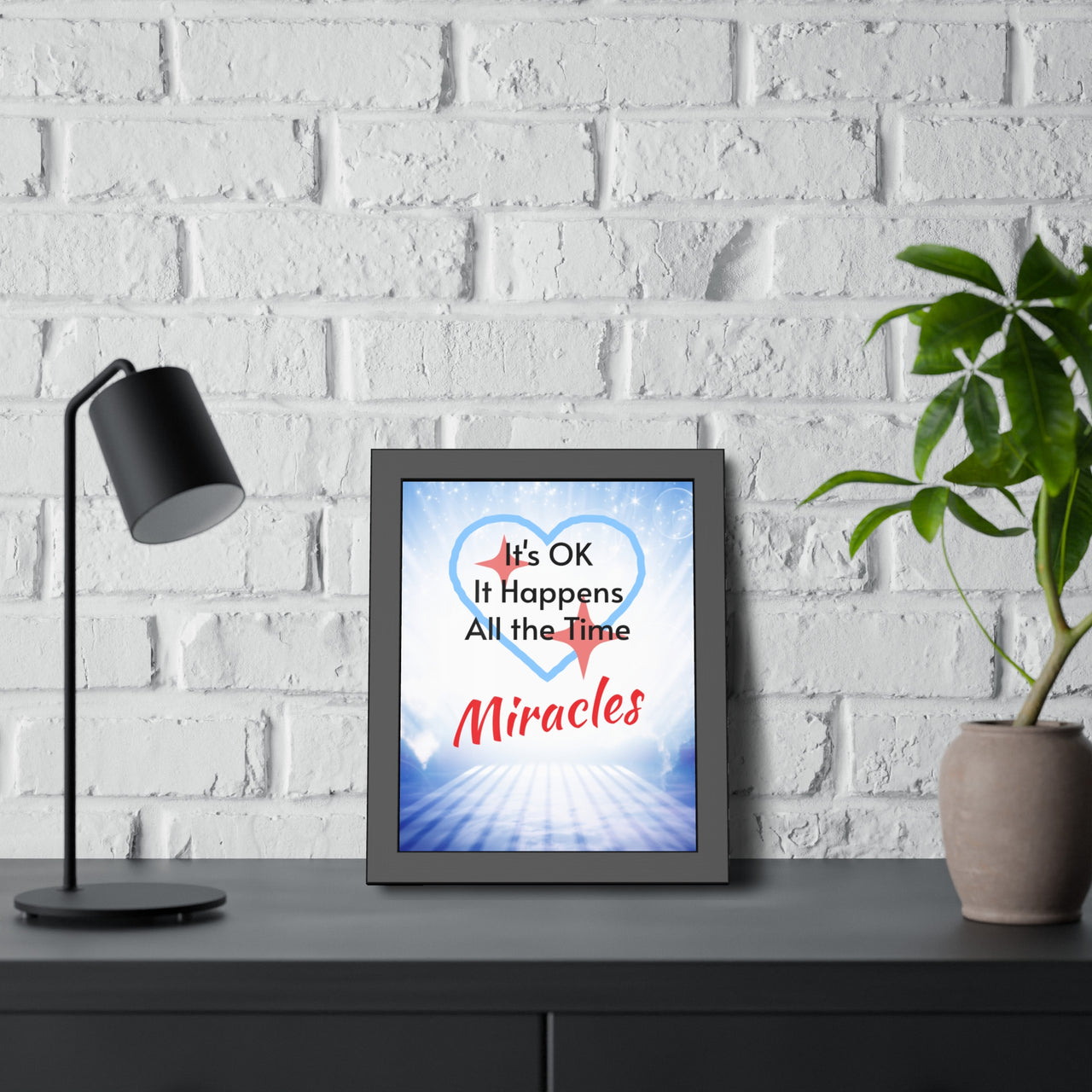 Black wood framed inspirational poster with “Miracles Happen” design with the message "It's Ok, It Happens All the Time - Miracles," semi-gloss finish, shatter-proof plexiglass, available in 3 sizes, faith-inspired wall art, 11x14 framed poster at desk
