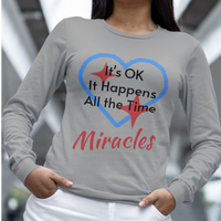 Long-sleeve Bella+Canvas t-shirt made from preshrunk ring-spun cotton with “Miracles Happen” design and message, “It’s OK. It Happens All the Time – Miracles,” faith-based apparel encouraging daily miracles through intimacy with God, woman wearing long-sleeve gray t-shirt