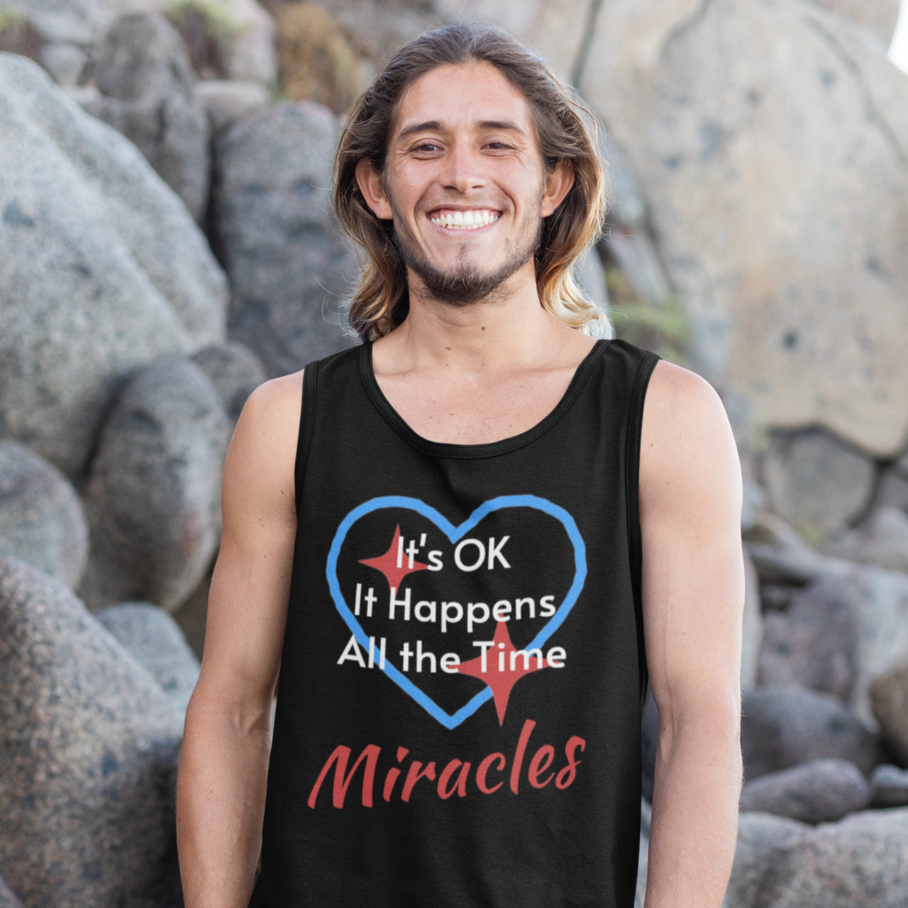 Lightweight Bella+Canvas tank top made from preshrunk cotton with “Miracles Happen” design message, “It’s OK. It Happens All the Time – Miracles,” inspirational apparel encouraging daily miracles through intimacy with God, man smiling by the rocks in black tank top