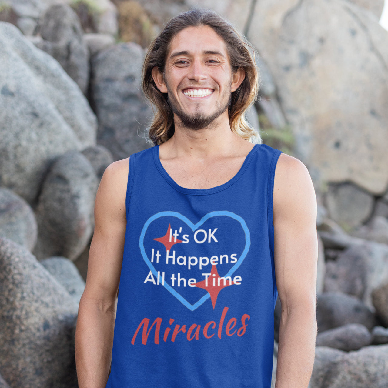 Lightweight Bella+Canvas tank top made from preshrunk cotton with “Miracles Happen” design message, “It’s OK. It Happens All the Time – Miracles,” inspirational apparel encouraging daily miracles through intimacy with God, man smiling at rockface wearing blue tank top