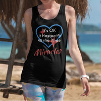 Lightweight Bella+Canvas tank top made from preshrunk cotton with “Miracles Happen” design message, “It’s OK. It Happens All the Time – Miracles,” inspirational apparel encouraging daily miracles through intimacy with God, 2nd woman at beach in black tank top
