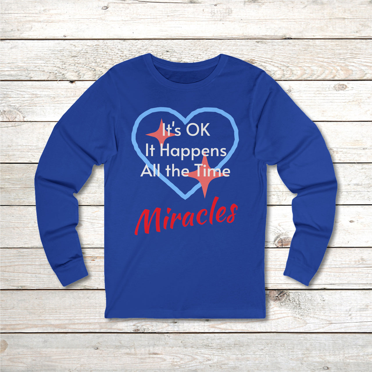Long-sleeve Bella+Canvas t-shirt made from preshrunk ring-spun cotton with “Miracles Happen” design and message, “It’s OK. It Happens All the Time – Miracles,” faith-based apparel encouraging daily miracles through intimacy with God, front of blue long-sleeve t-shirt