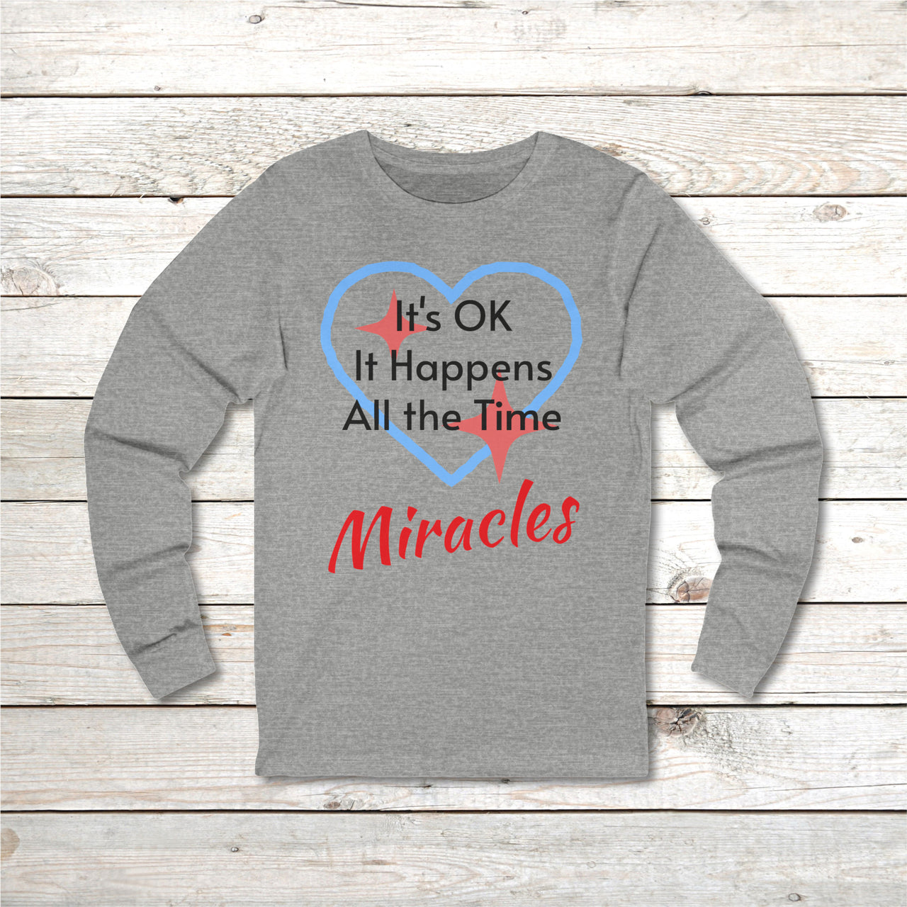 Long-sleeve Bella+Canvas t-shirt made from preshrunk ring-spun cotton with “Miracles Happen” design and message, “It’s OK. It Happens All the Time – Miracles,” faith-based apparel encouraging daily miracles through intimacy with God, front of gray long-sleeve t-shirt