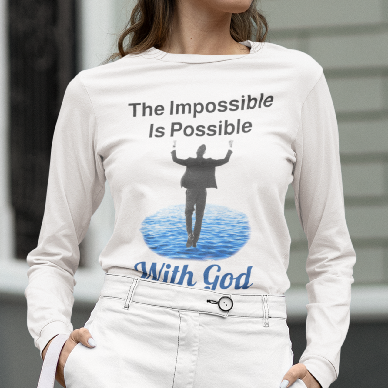 Long-sleeve Bella+Canvas t-shirt made from preshrunk ring-spun cotton with “Impossible Man” design message, “The Impossible Is Possible with God,” inspirational apparel calling believers to step out in faith and trust God for more than they can ask or imagine, woman wearing white long-sleeve t-shirt