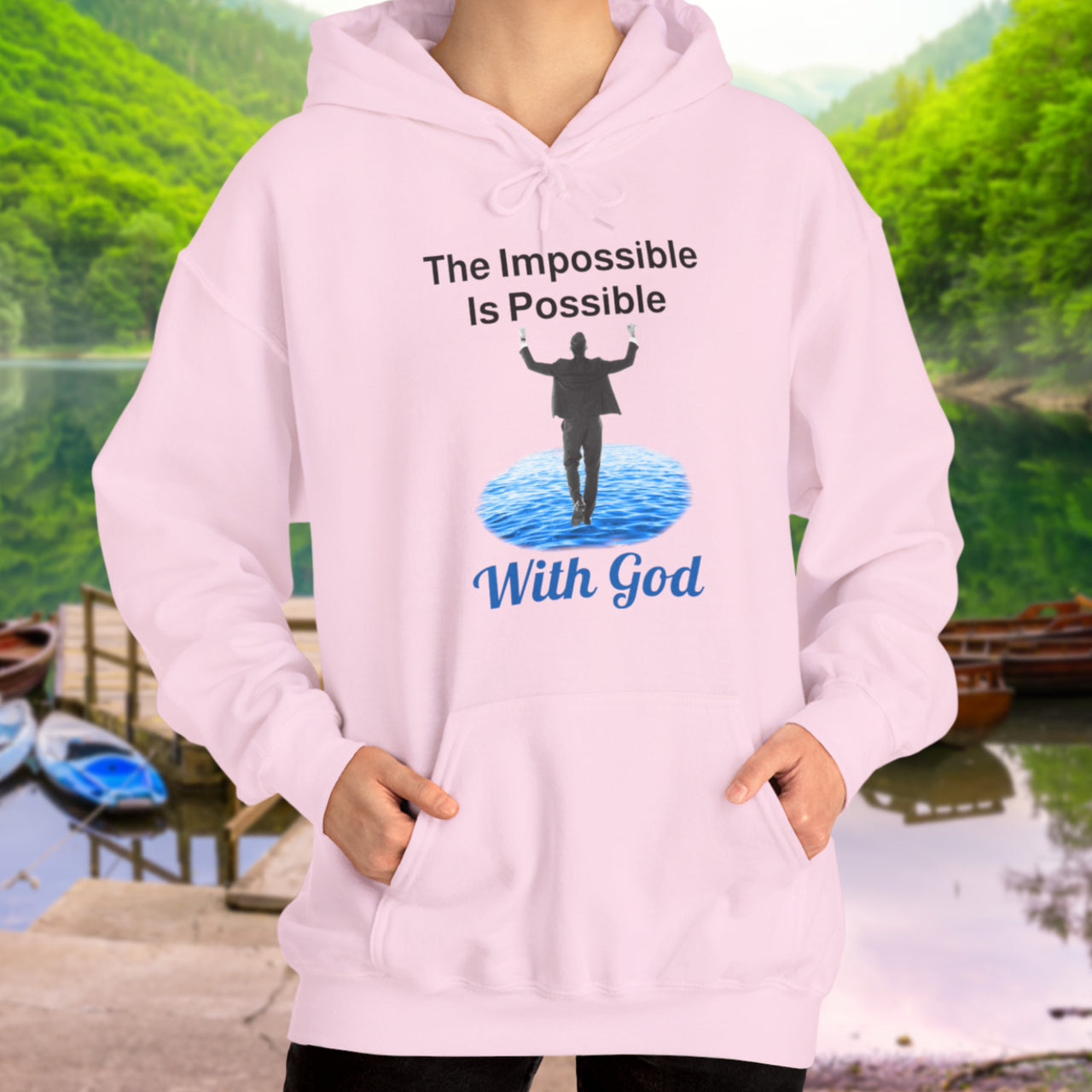 Gildan unisex hoodie with “Impossible Man” design featuring a man walking on water and uplifting message, Christian apparel made from soft cotton-poly blend, perfect for cold weather and spiritual encouragement, woman in pink hoodie
