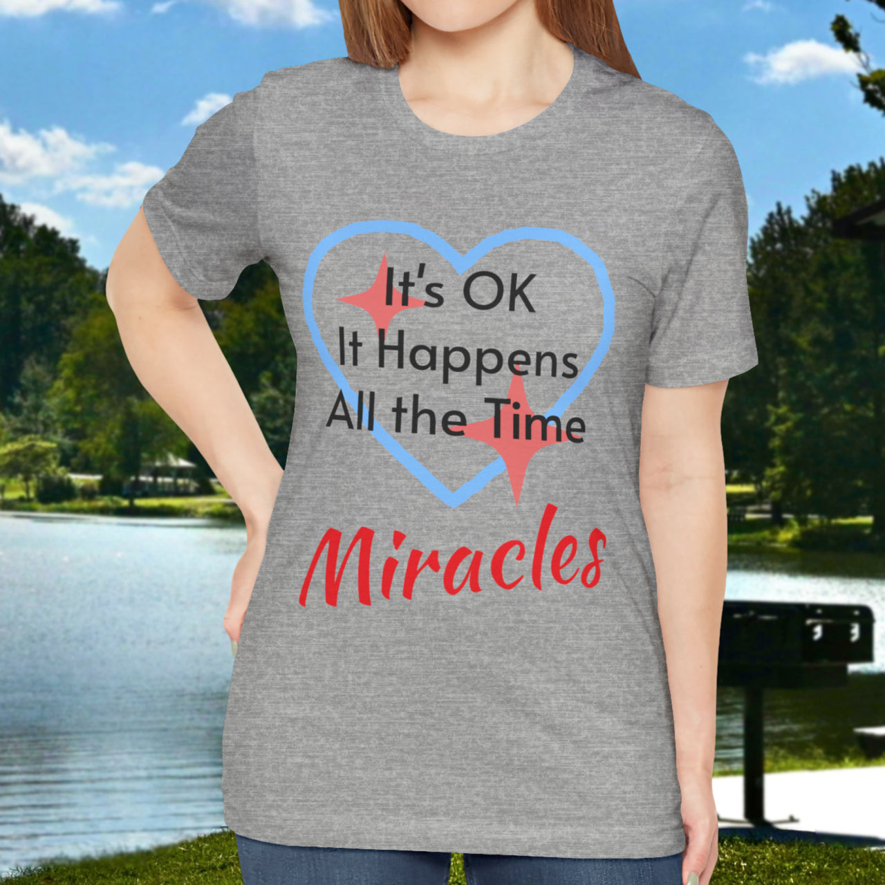 Soft, breathable Bella+Canvas t-shirt made from preshrunk cotton with “Miracles Happen” design message, “It’s OK. It Happens All the Time – Miracles,” inspirational shirt encouraging intimacy with God that produces everyday miracles, woman in gray shirt