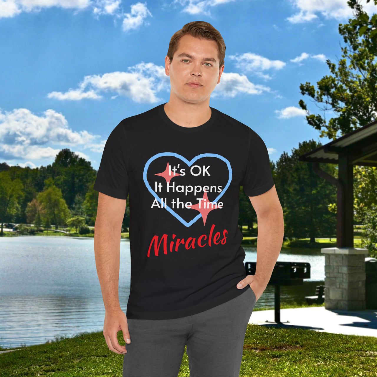 Soft, breathable Bella+Canvas t-shirt made from preshrunk cotton with “Miracles Happen” design message, “It’s OK. It Happens All the Time – Miracles,” inspirational shirt encouraging intimacy with God that produces everyday miracles, man wearing black t-shirt at lakeside park