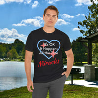 Soft, breathable Bella+Canvas t-shirt made from preshrunk cotton with “Miracles Happen” design message, “It’s OK. It Happens All the Time – Miracles,” inspirational shirt encouraging intimacy with God that produces everyday miracles, man wearing black t-shirt at lakeside park