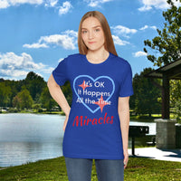 Soft, breathable Bella+Canvas t-shirt made from preshrunk cotton with “Miracles Happen” design message, “It’s OK. It Happens All the Time – Miracles,” inspirational shirt encouraging intimacy with God that produces everyday miracles, woman in blue t-shirt at lakeside park