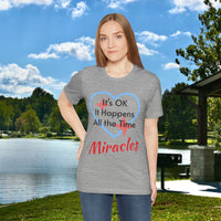 Soft, breathable Bella+Canvas t-shirt made from preshrunk cotton with “Miracles Happen” design message, “It’s OK. It Happens All the Time – Miracles,” inspirational shirt encouraging intimacy with God that produces everyday miracles, woman in gray t-shirt at lakeside park