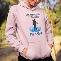 Gildan youth unisex hoodie with “Impossible Teen” design featuring a teen walking on water and uplifting message, Christian apparel made from soft preshrunk fleece, perfect for cold weather and spiritual encouragement, girl in pink hoodie