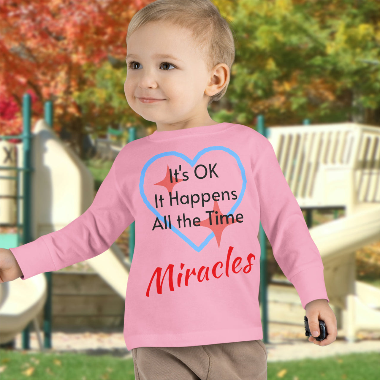 Rabbit Skins toddler long-sleeve t-shirt with “Miracles Happen” design and uplifting message, soft cotton, breathable and durable, Christian apparel for everyday wear and faith-filled gifting, todder boy in pink long-sleeve t-shirt