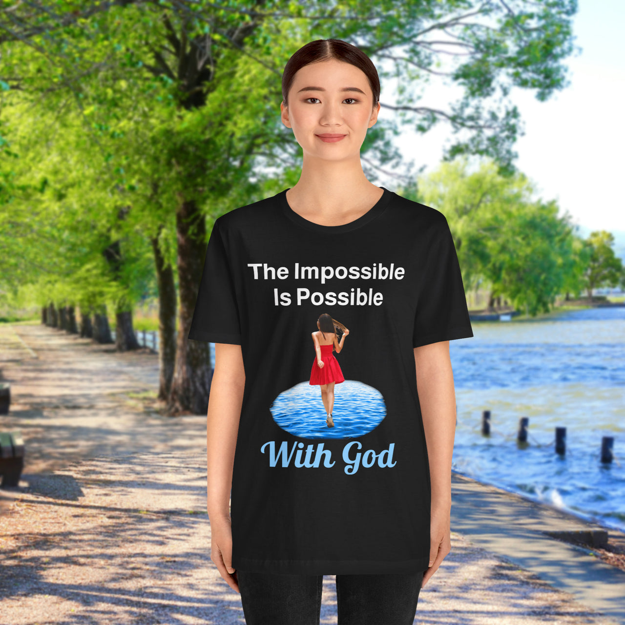 Soft, breathable Bella+Canvas t-shirt made from preshrunk cotton with “Impossible Woman” design message, “The Impossible Is Possible with God,” inspirational shirt encouraging bold obedience and faith-filled movement with God, Asian woman in black t-shirt at waterside walkway