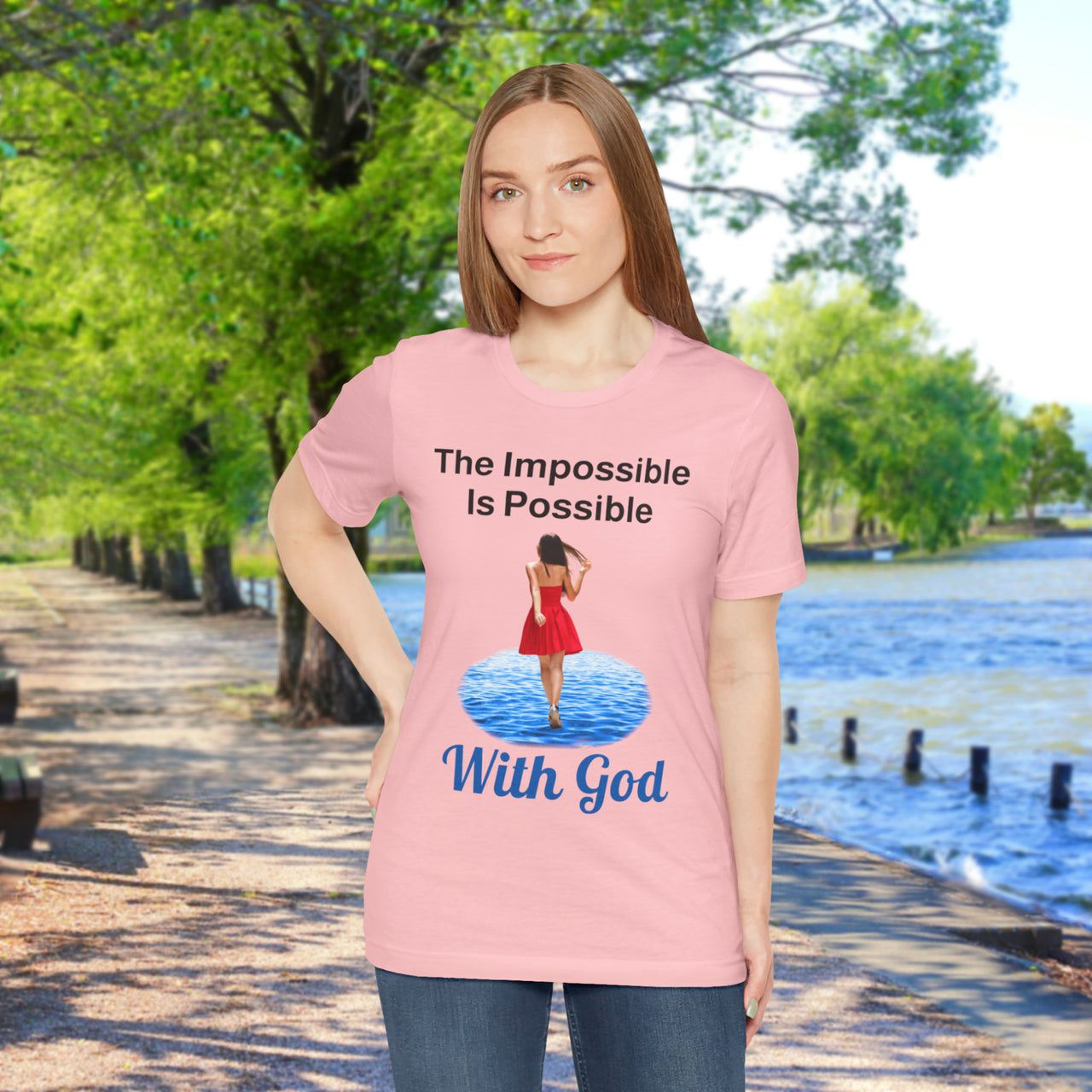 Soft, breathable Bella+Canvas t-shirt made from preshrunk cotton with “Impossible Woman” design message, “The Impossible Is Possible with God,” inspirational shirt encouraging bold obedience and faith-filled movement with God, woman in pink t-shirt at waterside walkway