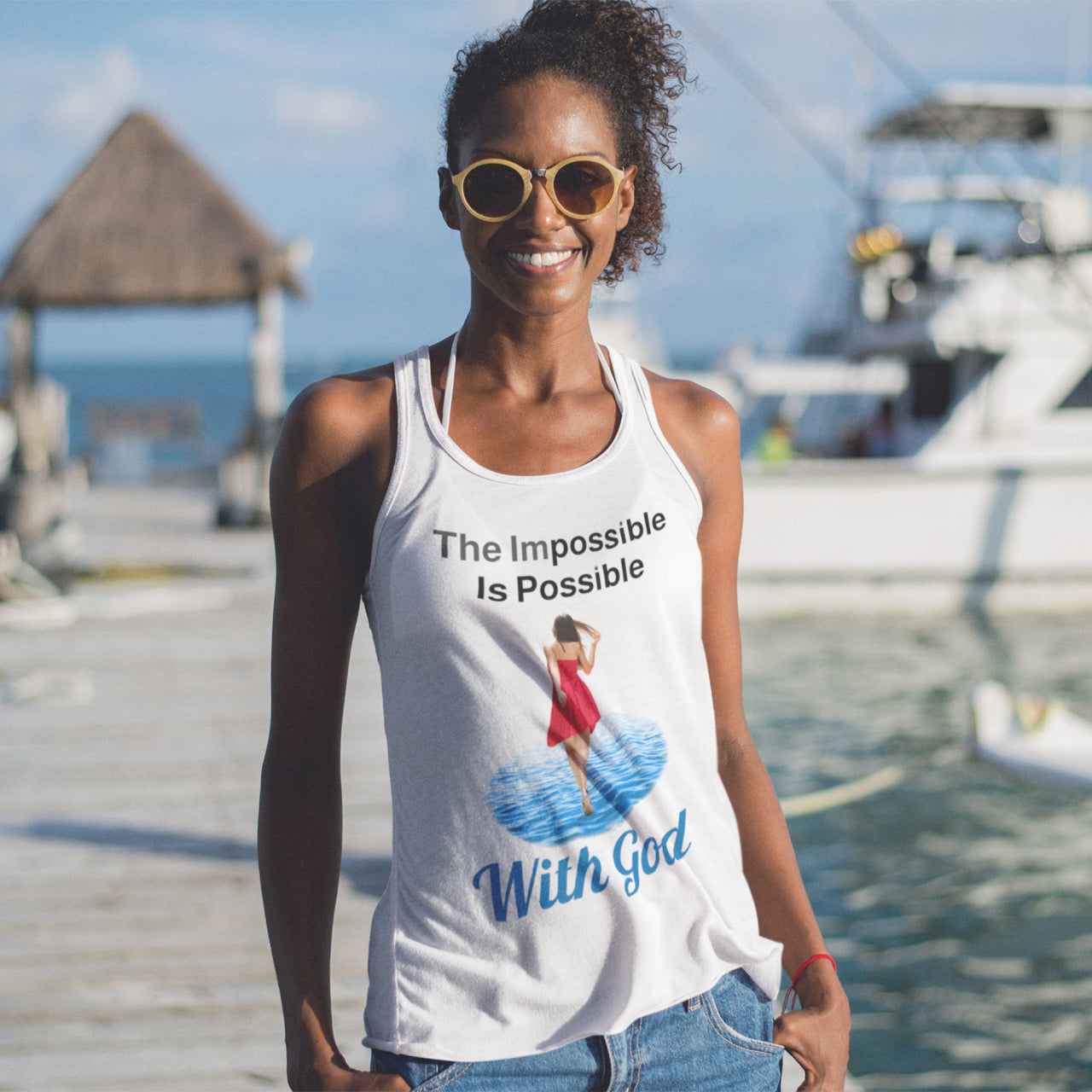 Lightweight Bella+Canvas tank top made from preshrunk cotton with “Impossible Woman” design message, “The Impossible Is Possible with God,” inspirational apparel encouraging women to walk in step with God who makes our impossible dreams become real, woman at the beach wearing white tank top