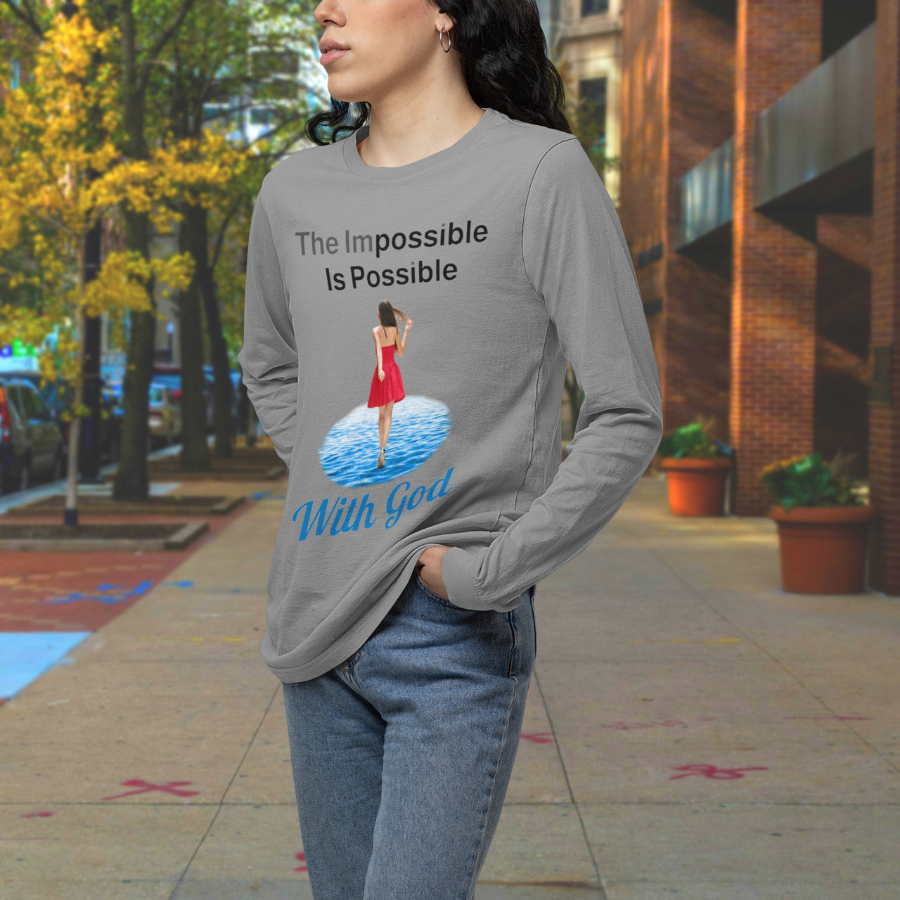 Long-sleeve Bella+Canvas t-shirt made from preshrunk ring-spun cotton with “Impossible Woman” design message, “The Impossible Is Possible with God,” inspirational apparel encouraging women to walk freely in God's incredible ways, woman downtown wearing gray long-sleeve t-shirt