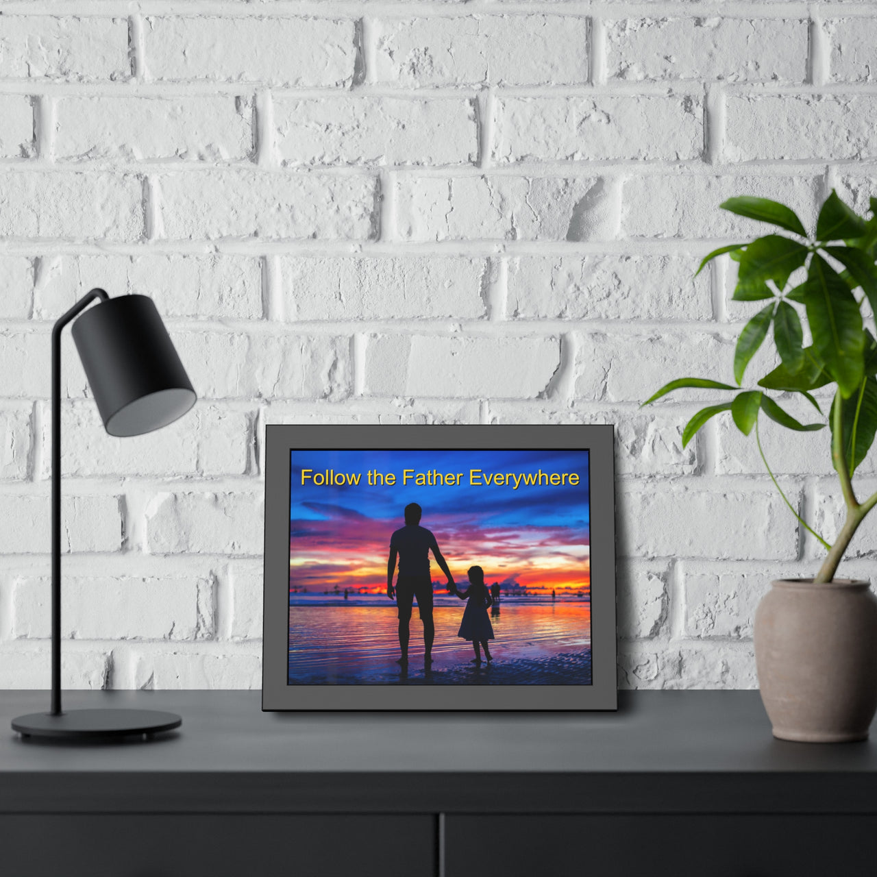 Black wood framed inspirational poster with “Follow the Father” design, child walking with father with the message "Follow the Father Everywhere," semi-gloss finish, shatter-proof plexiglass, available in 3 sizes, 14x11 framed poster at desk