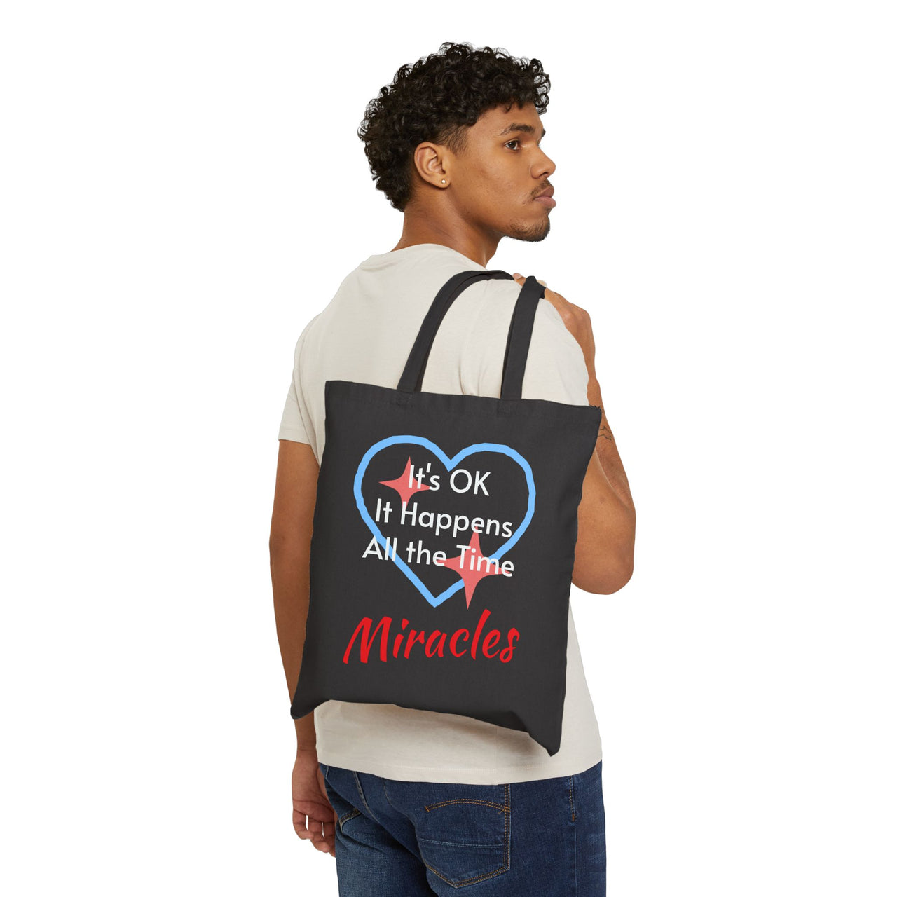 Cotton canvas tote bag with "Miracles Happen" design, message “It’s OK. It Happens All the Time – Miracles,” printed on both sides, durable faith-based tote bag for everyday encouragement of God's goodness, man carrying black tote bag