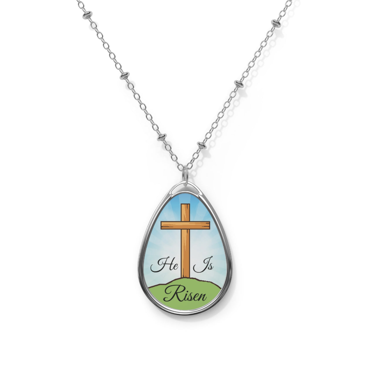 Inspirational oval pendant necklace with "He Is Risen" design,  cross on a hill artwork, zinc alloy and white aluminum, spiritual jewelry for resurrection faith, blue sky - front