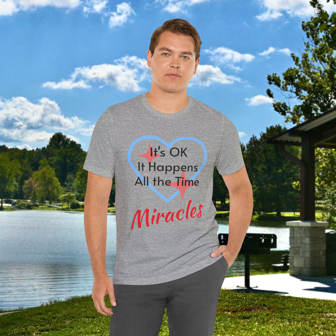 Soft, breathable Bella+Canvas t-shirt made from preshrunk cotton with “Miracles Happen” design message, “It’s OK. It Happens All the Time – Miracles,” inspirational shirt encouraging intimacy with God that produces everyday miracles, man in gray t-shirt at lakeside park
