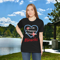 Soft, breathable Bella+Canvas t-shirt made from preshrunk cotton with “Miracles Happen” design message, “It’s OK. It Happens All the Time – Miracles,” inspirational shirt encouraging intimacy with God that produces everyday miracles, woman wearing black t-shirt at lakeside park