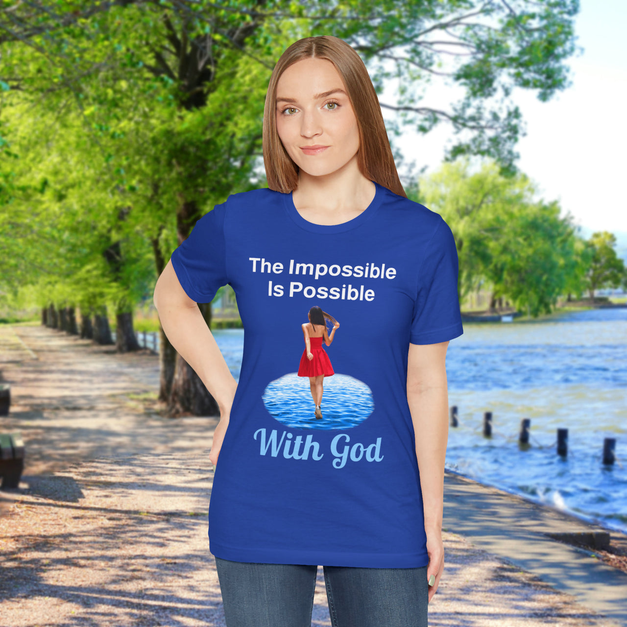 Soft, breathable Bella+Canvas t-shirt made from preshrunk cotton with “Impossible Woman” design message, “The Impossible Is Possible with God,” inspirational shirt encouraging bold obedience and faith-filled movement with God, woman in blue t-shirt at waterside walkway