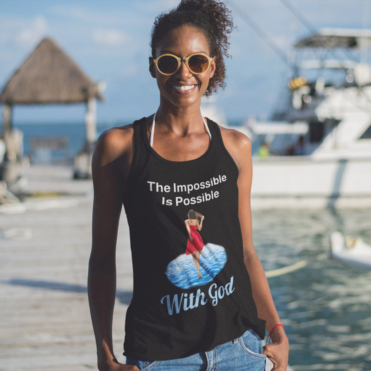 Lightweight Bella+Canvas tank top made from preshrunk cotton with “Impossible Woman” design message, “The Impossible Is Possible with God,” inspirational apparel encouraging women to walk in step with God who makes our impossible dreams become real, woman at beach wearing black tank top
