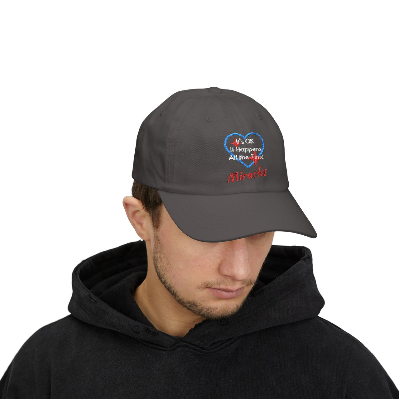Classic cotton baseball cap with "Miracles Happen" design, message “It’s OK. It Happens All the Time – Miracles,” adjustable fit, spiritual hat for everyday encouragement, man wearing gray cap