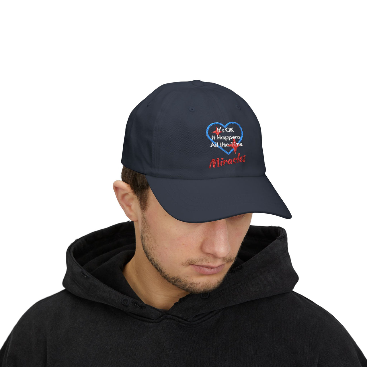 Classic cotton baseball cap with "Miracles Happen" design, message “It’s OK. It Happens All the Time – Miracles,” adjustable fit, spiritual hat for everyday encouragement, man wearing navy cap